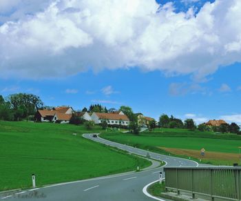 Road passing through field against cloudy sky