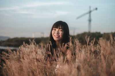 Portrait of smiling young woman standing on field against sky