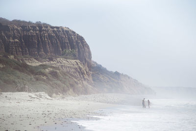 Family at beach by cliff against clear sky