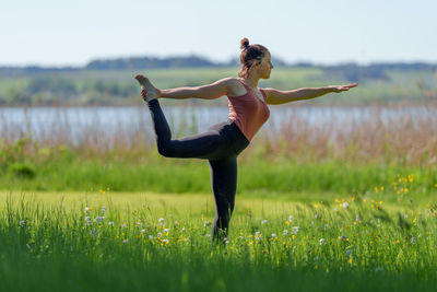 Woman doing yoga poses outdoors in summer near lake