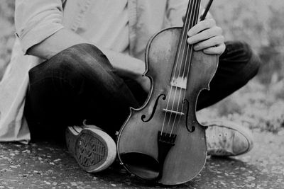 Low section of man holding violin while sitting outdoors