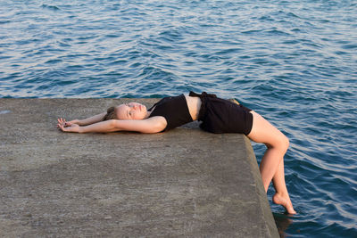 A young girl in black clothes is lying on the sea pier