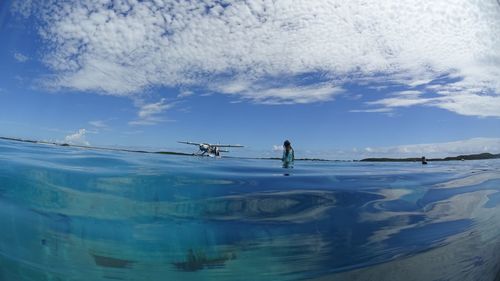 Surface level of sea with woman and seaplane in background against cloudy sky