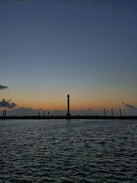 Silhouette buildings by sea against sky during sunset