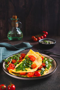 French omelette filled with cherry tomatoes and arugula on a plate on the table vertical view