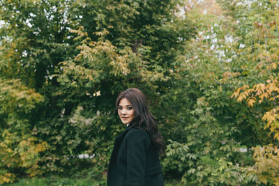 Portrait of a smiling young woman standing against plants