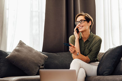 Woman using mobile phone while sitting on sofa at home