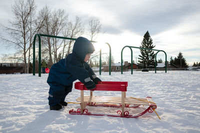Young boy pushing a sled on a snowy hill