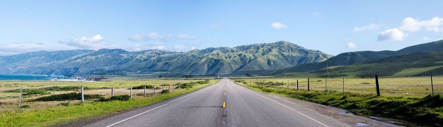 Empty road by mountains against sky