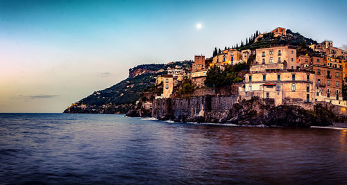 Buildings by sea against sky at dusk