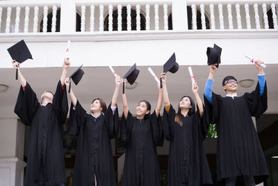 Students in university gowns holding mortarboards while standing against building