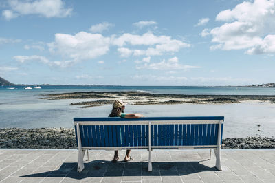 Young woman looking at view while sitting on bench during sunny day