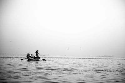 Men rowing in lake against sky