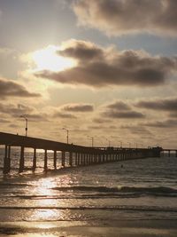 Silhouette bridge over sea against sky during sunset