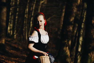 Young woman standing against tree trunk in forest