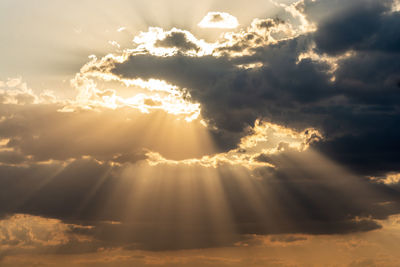 Low angle view of sunlight streaming through clouds during sunset