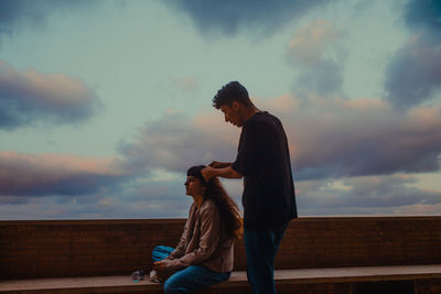 Side view of couple sitting against sky