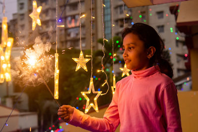 Side view of girl holding illuminated string lights at night