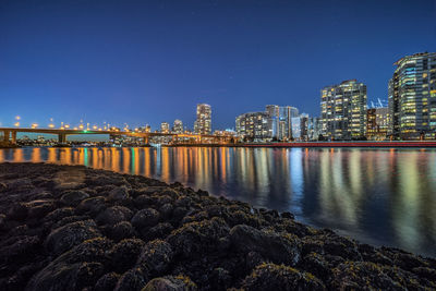 Illuminated buildings by sea against clear sky at night