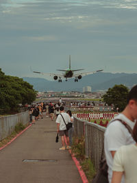 Rear view of people at airplane against sky