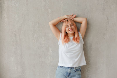 Portrait of smiling young woman standing against wall