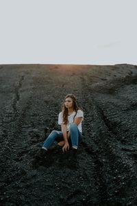 Portrait of young woman sitting on land against sky