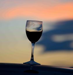 Close-up of wineglass against sky during sunset