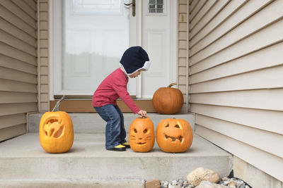 Side view of baby boy holding jack o lantern while standing at entrance