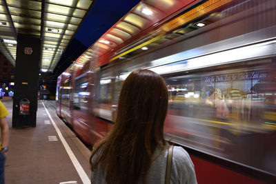 Rear view of woman looking at speeding train at railroad station