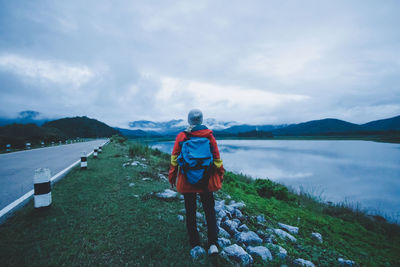 Rear view of man standing by lake against sky