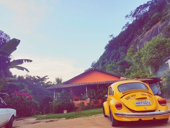 Yellow car on road by trees against sky