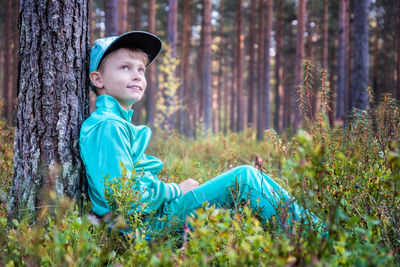 Cute boy sitting on grassy field at forest