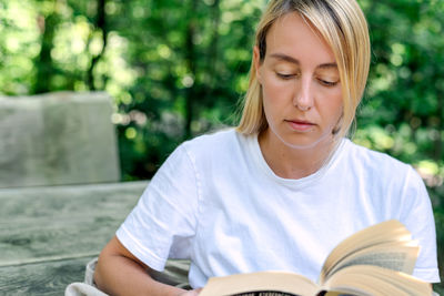 A young woman reads a book outdoors.