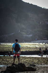 Rear view of men standing on rock by sea