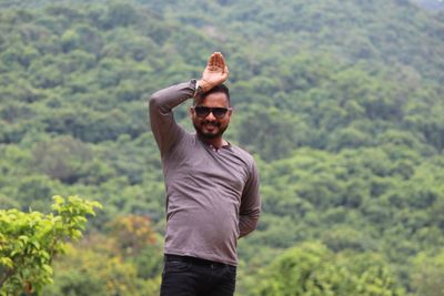 Young man wearing sunglasses standing against plants