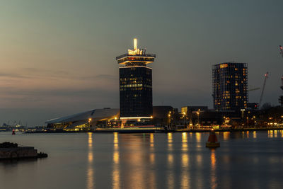Illuminated buildings by sea against sky at night
