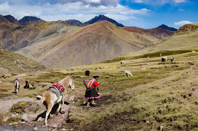 Side view of woman with horse walking on mountain against sky