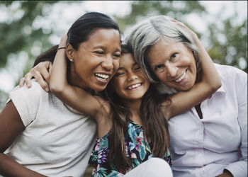 Portrait of happy girl embracing mother and grandmother at yard