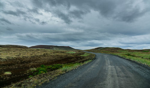 Country road amidst landscape against sky