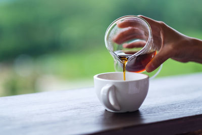 Closeup image of a hand pouring drip coffee into a white mug with blurred nature background