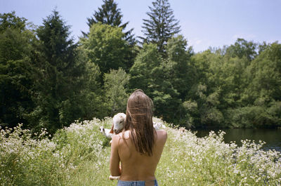 Rear view of topless woman holding goat with trees in background