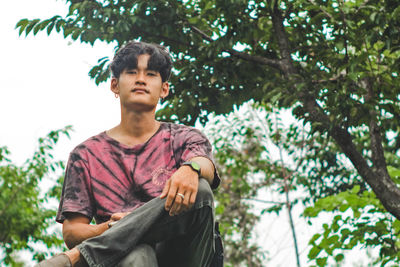 Portrait of young man sitting on tree