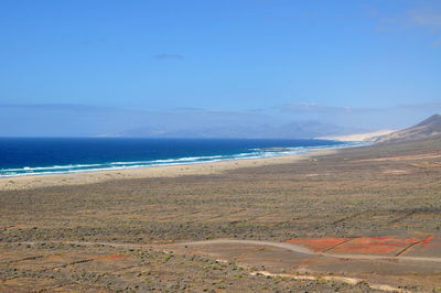 Scenic view of landscape by sea against blue sky