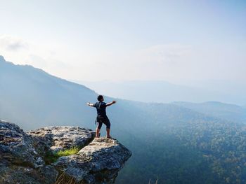 Man standing on rock looking at mountain range against sky