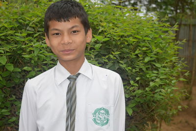 Portrait of smiling young man wearing school uniform standing against plants