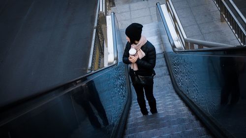 Full length of woman holding disposable cup while standing on escalator