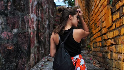 Rear view of young woman standing on footpath amidst walls