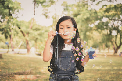 Cute girl blowing bubbles while standing on field