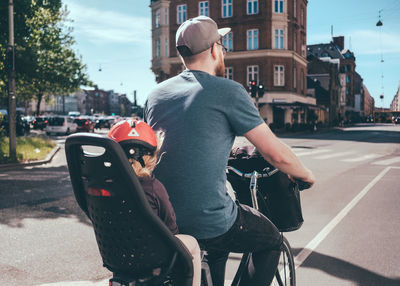 Rear view of father cycling while daughter sitting on back seat at city street