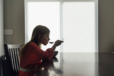 Side view of girl eating food while sitting at home